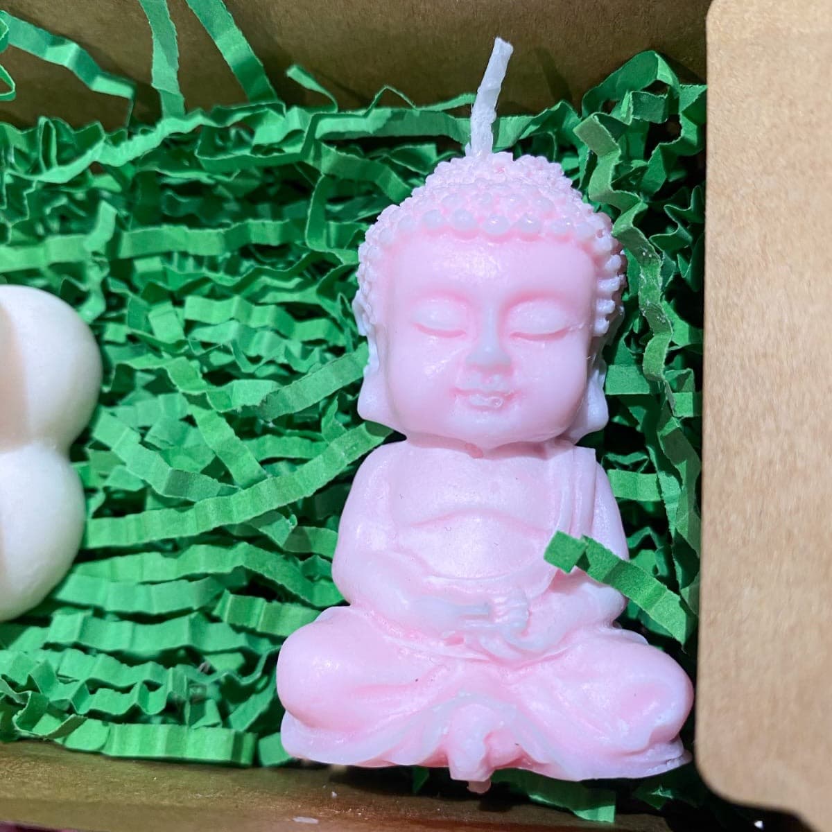 Soft pink Buddha candle sitting in a kraft gift box with green paper