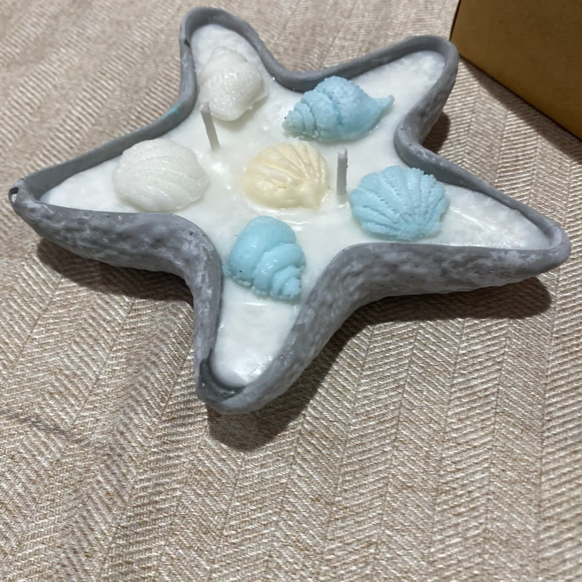 Star-shaped candle with grey rim and white wax, decorated with wax seashells