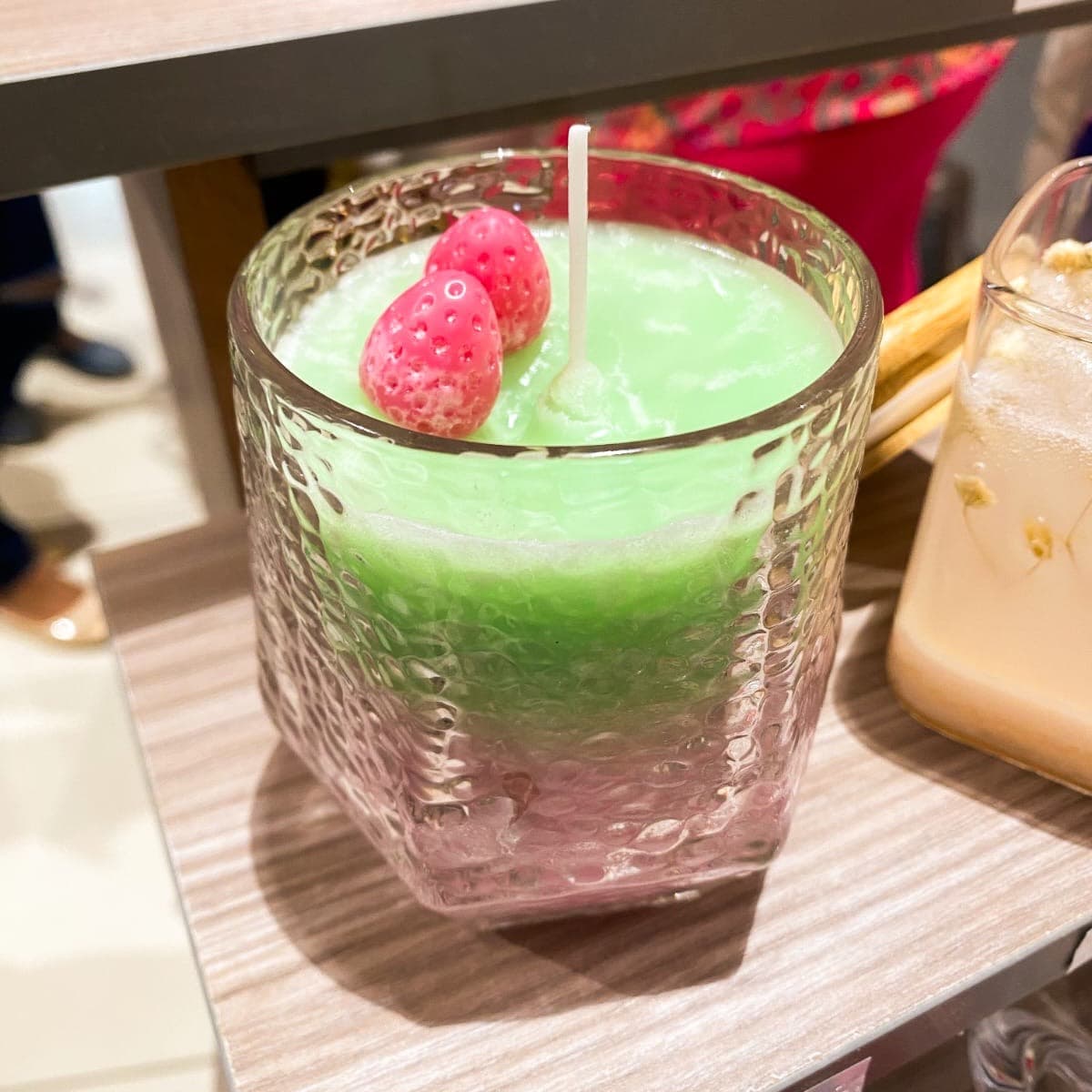 Strawberry Matcha candle — green wax with two wax strawberries in a frosted glass